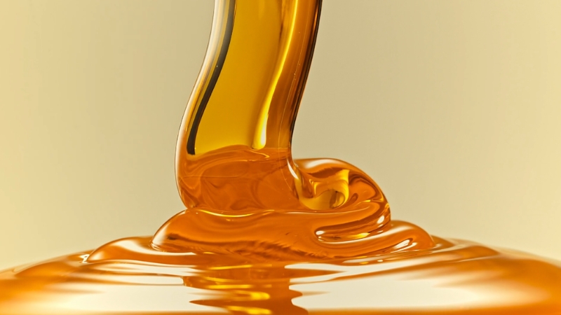 Gust mlaz zlatnog meda koji se sliva i pravi sjajnu, glatku površinu