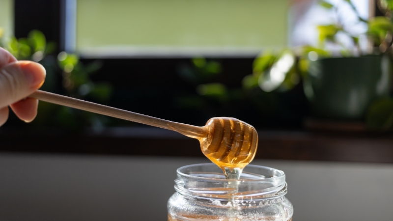 Kašika za med dok se zlatni med sliva u staklenu teglu