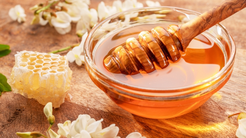 Staklena činija sa zlatnim bagremovim medom i drvenom kašikom